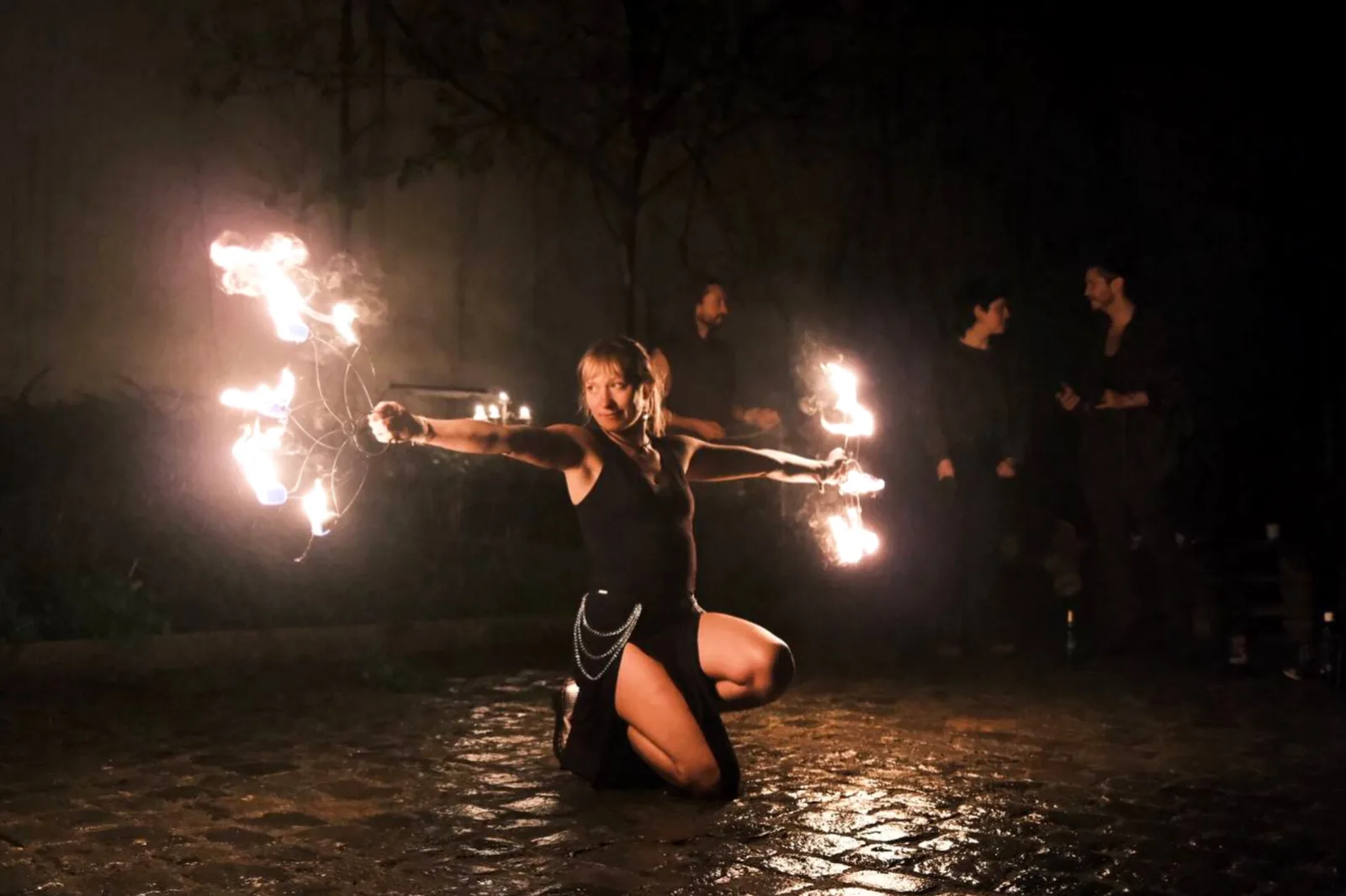 Performer kneeling with two burning fire fans spread wide
