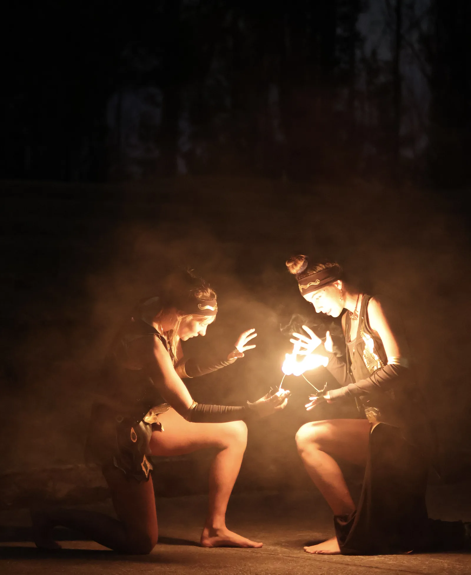 Two performers close together shaping a small flame between their hands