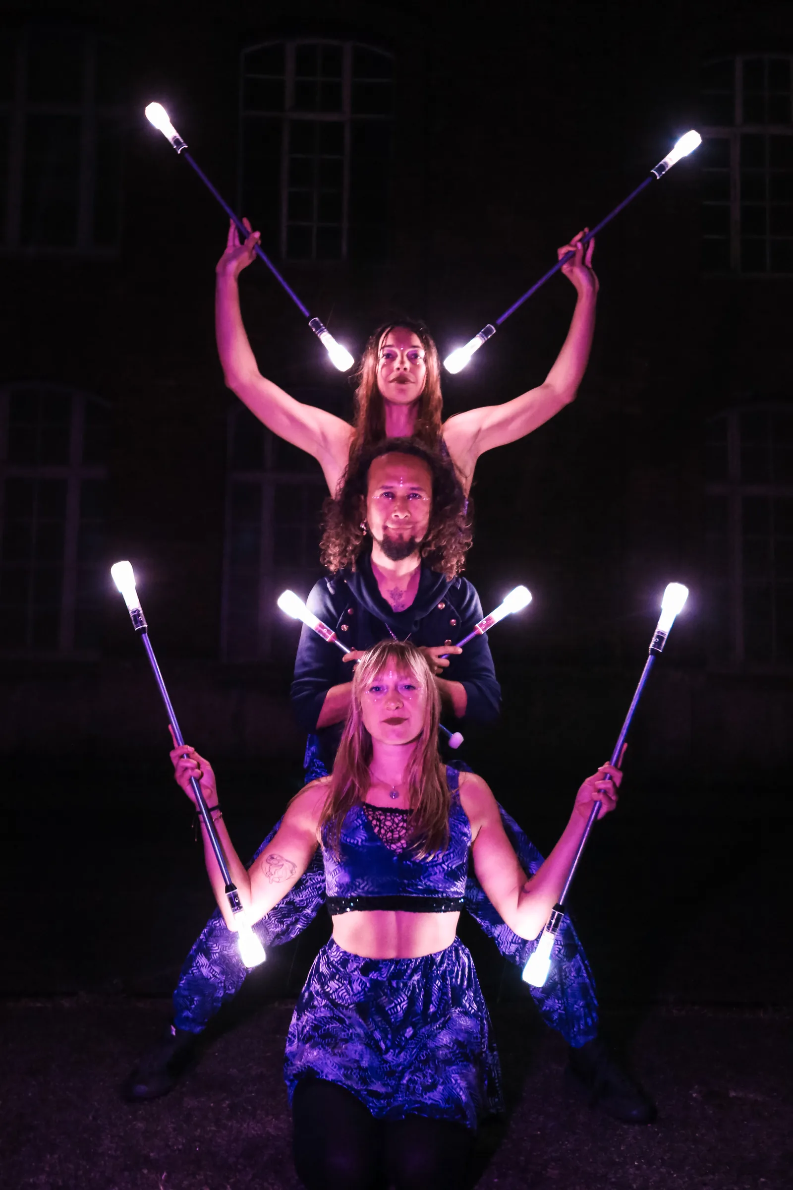 Three performers with glowing LED staffs in violet light